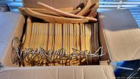 Open cardboard box filled with stacked wooden children's hangers, showing the metal hooks and slim design.