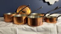Five copper pans of varying diameters arranged front to back with lid behind
