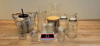 Lot of various clear glass containers, vases, heavy glass bucket with metal handle, and a digital scale on wooden floor