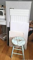 Overall view of four backdrop boards stacked vertically with a small round distressed wooden stool in front on hardwood floor.