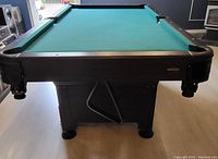 Front view of the compact pool table showing green felt playing surface, dark wood frame, and robust legs