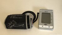 Blood pressure monitor with attached cuff and part of carrying case visible.