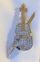 Front view of gold-tone violin brooch with a clear rhinestone decorated body and an attached bow detail on fabric background.