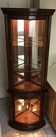 Full view of the corner curio cabinet with lights on upper and lower sections, wood finish with glass doors.