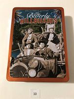 Front of the Beverly Hillbillies Collector's Edition tin box showing the main characters in sepia tone sitting on an old vehicle, with the title embossed at the top.