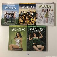 Front covers of the DVD cases for Weeds Seasons 1 through 5, showing cast and themed imagery.