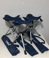 Three navy blue Eureka camp stools folded with their carrying cases on a white surface.