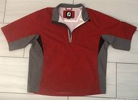 Front view of FootJoy Dryjoys Hydro Lite short sleeved rain shirt/jacket showing red fabric body with grey panels and black underarms, half zipper, and collar.