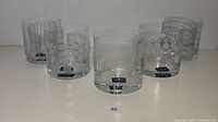 Front view of five Mikasa Cheers Double Old Fashioned glasses arranged in a row, showing clear glass with varied decorative patterns, four glasses have Mikasa labels.