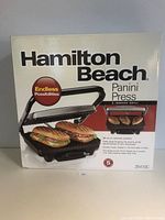 Front view of the Hamilton Beach Panini Press in original sealed box showing the product image and key features.
