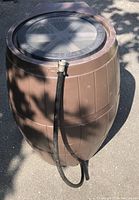 Brown Series 4000 Raincatcher rain barrel with attached black hose, showing side profile and flat back.