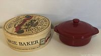 Red ceramic Brie Baker next to its original cardboard box labeled Petit Maison Brie Baker
