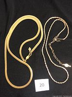Two gold-tone necklaces on black background, one adjustable flat chain and one twisted chain necklace.