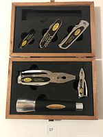 Open keepsake box containing six stainless steel multi-tools and a small flashlight, organized in foam insert.