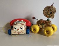 Front view of vintage Fisher Price Prancy Pony and Chatter Telephone toys showing the horse figure on yellow wheels and smiling rotary telephone with red handset and blue wheels.