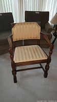 Full view of antique wooden armchair showing carved legs, armrests, and upholstered seat and back in gold striped fabric.