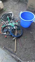 Entire garden tools lot showing multiple items including lopper, saw, edging tools, hoses, and bucket on dirt floor