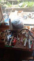 Overview of garden and hand tools on wooden table including saw, shears, gloves