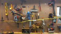 Wide view of pegboard with various hand tools including clamps, levels, staplers, scissors, and a leather tool belt hung on hooks.