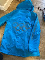 Blue jacket with hood, back view showing gold Olympic rings and 'Vancouver 2010' on sleeve