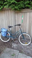Full side view of the dark blue lady's cruiser bike showing step-through frame, whitewall tires, rear rack with blue saddle bags, and extended handlebar stem.