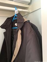 Joseph and Feiss black jacket with beige inner lining hanging on a blue hanger.