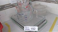 Stack of 4 clear glass Pyrex measuring cups on top of a large glass rectangular baking dish with handle. Two additional glass rectangular baking dishes underneath.