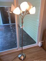 Full view of the brushed nickel floor lamp with five white conical shades, placed near a glass door.