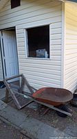 Wheelbarrow positioned outside near a siding wall with folding sand screen leaning against it