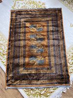 Top view of small rectangular area rug with blue and black abstract geometric patterns on brown background, showing the entire rug and some fringes at one edge.