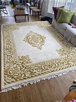 Full view of large cream-colored area rug with green and beige floral and scroll patterns, placed on wooden floor in living room area.