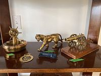 Overview of all items including brass ashtray with ship wheel, brass panther, brass canon on wood base, brass medallion, and blue toy train.
