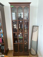 Front view of full tall wooden display cabinet with glass front divided into multiple panes. Contents inside not included.