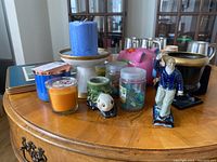 Overview of assorted home décor items on wooden surface showing candles, piggy bank, figurine, and placemats