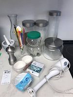 Overview of all items including canisters, immersion blender, pepper mill, mortar and pestle, swizzle sticks, cupcake liners, coffee filters, and cleaning cloths on marble countertop.