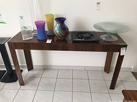 Front view of wood console table with various glass items placed on top, showing its length and design.