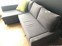 Full side-angle view of two-piece grey sleeper couch with green throw pillow showing condition.