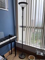 Full view of the floor lamp standing next to a keyboard and window showing its overall height and form.