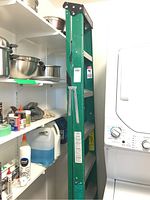 Side view of the green Louisville step ladder leaning against the wall between shelving and a laundry machine, showing the ladder height and step detail.