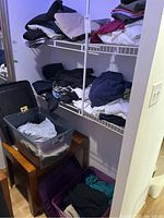Three shelves filled with men's folded casual clothing and two plastic bins on table and floor