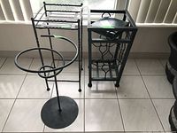 Photo showing three metal plant stands varying in shape and size: round base stand, rectangular stand with shelf, square stand with decorative sides.