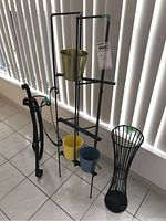 Three metal plant stands and 3 pots including tall multi-level stand with three pots, curved short stand, and slender basket-style stand on tile floor