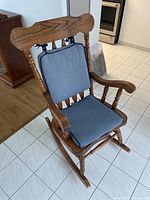 Front view of wooden rocking chair with blue seat and back cushions on tiled floor.