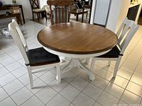 Photo showing full view of round wood table and two matching chairs with black seat cushions