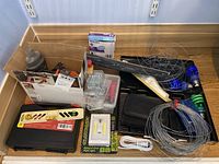 Box with assorted tools and hardware including coils of wire, soldering iron, measuring tape, screws, and small hand tools.