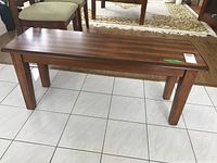 Wooden bench shown on white tile floor with visible legs, flat seat, and medium brown wood finish.