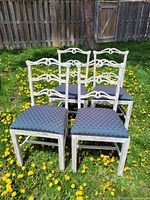 Four white shabby chic dining chairs with decorative backs and emerald/ruby patterned fabric seats arranged on grass outdoors.