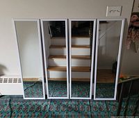 Four tall rectangular white framed wall mirrors standing upright against a wall showing full height and width.