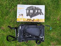 Front view of black Sherpa pet carrier with original packaging box placed behind on grass.