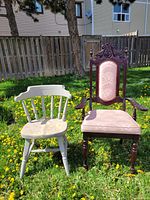 Two chairs photographed outdoors on grass with dandelions: grey painted wooden chair with a natural wood seat and an ornate princess style wooden chair with carved details and pink upholstery.